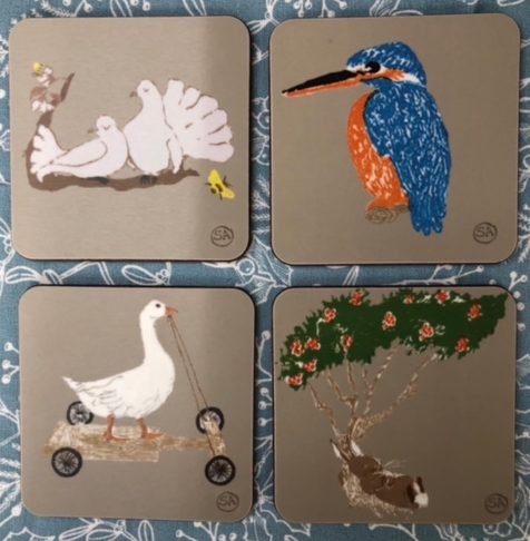 four new coaster designs from sal - doves, a kingfisher, a goose go-carting, a rabbit resting under a rowan tree. All on a light grey melamine background, cork backing.