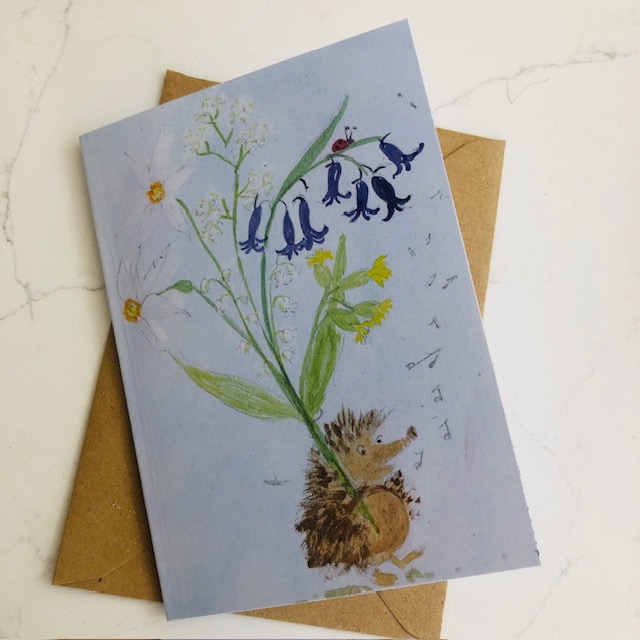 A hedgehog is singing along carrying you a large bunch of flowers he has picked for whoever receives this greetings card: bluebells, pheasant eye narcissi, cowslips, cow parsley and lily-of-the-valley